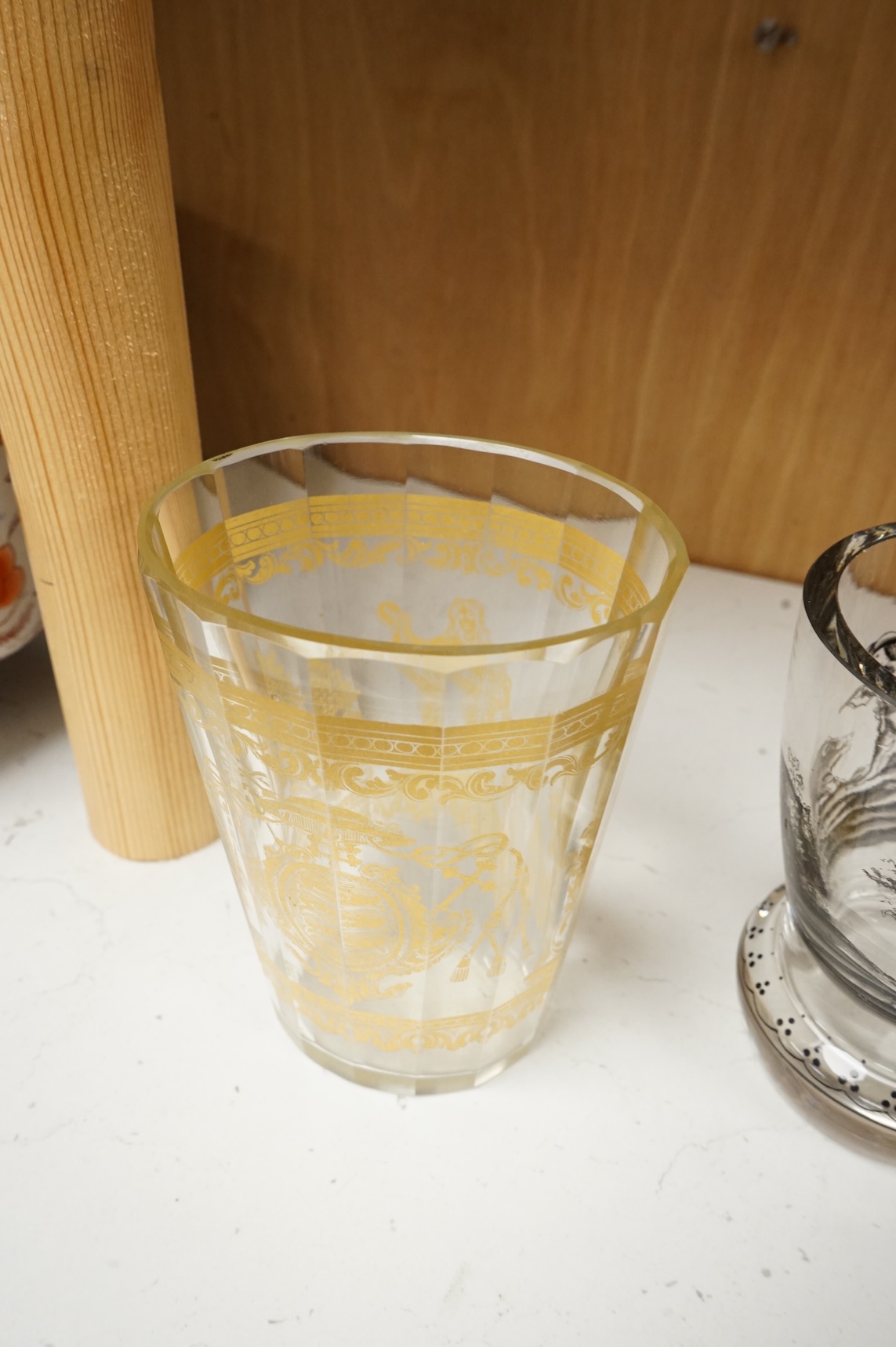 An Italian gilt-decorated and faceted beaker, inscribed Daniel Delvinis, the reverse with papal coat of arms, and a German Schwarzlot black enamelled ‘hunting’ beaker, largest 12cm (2)